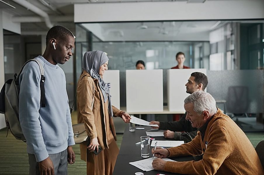 A diverse group of adults engaged in voting at an indoor polling station — legat de Politica extrema dreapta